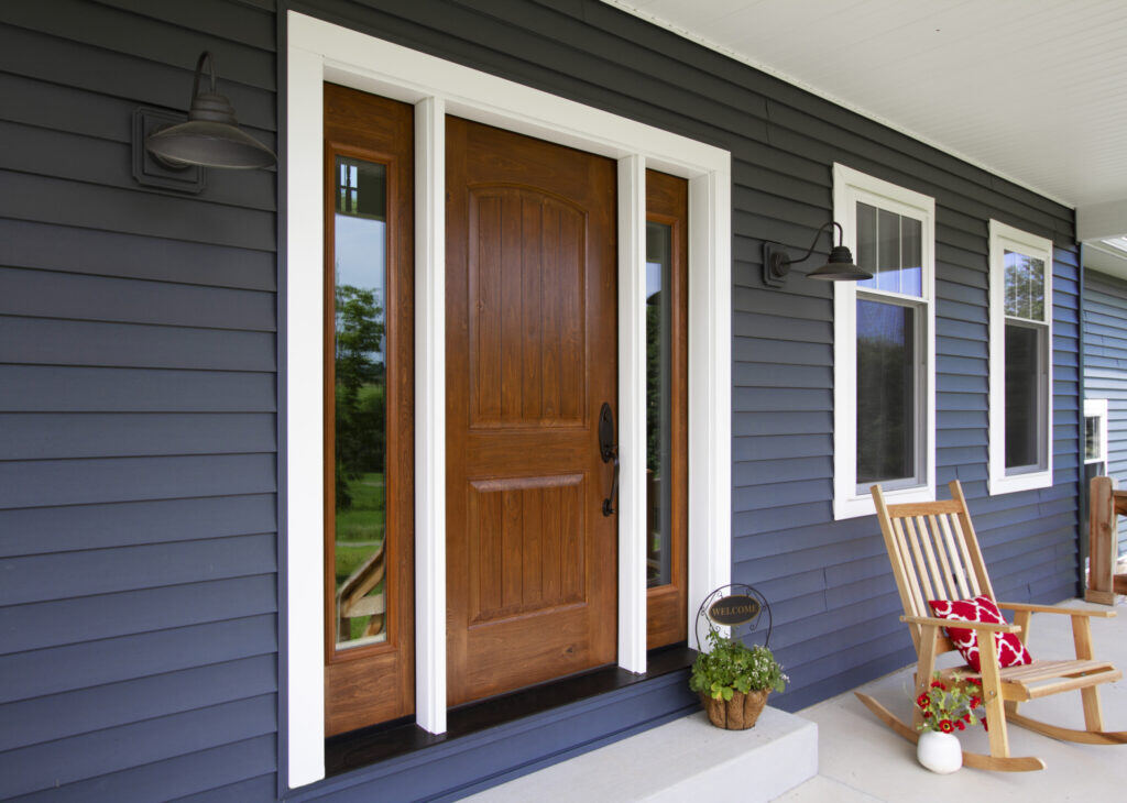 Close-up of an installed brown door on the porch of a blue house.